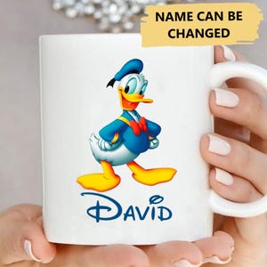 May include: White ceramic mug featuring a cartoon image of Donald Duck wearing a blue sailor shirt and a red bow tie. The name "DAVID" is printed in blue below the image.