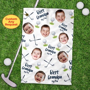 May include: White golf towel with a repeating pattern of smiling children's faces, golf balls, and crossed golf clubs. The words "Best Grandpa by Par" are printed in navy blue. A golf putter and golf balls are in the background.