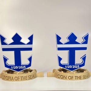 Peut inclure: Deux mod&egrave;les imprim&eacute;s en 3D du logo de Royal Caribbean International, en bleu et blanc. Le logo repr&eacute;sente une couronne, une lettre T et une ancre. Le mod&egrave;le de gauche indique "Utopia of the Seas" et le mod&egrave;le de droite indique "Icon of the Seas". Les deux mod&egrave;les portent la date "1/20/2025".
