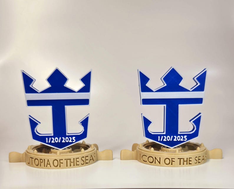 Peut inclure: Deux mod&egrave;les imprim&eacute;s en 3D du logo de Royal Caribbean International, en bleu et blanc. Le logo repr&eacute;sente une couronne, une lettre T et une ancre. Le mod&egrave;le de gauche indique "Utopia of the Seas" et le mod&egrave;le de droite indique "Icon of the Seas". Les deux mod&egrave;les portent la date "1/20/2025".