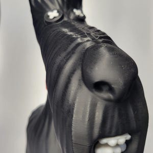 May include: A black sculpture of a dog's head with white accents. The dog has a long snout, large nose, and open mouth with white teeth. The eyes are white crosses. The sculpture is likely 3D-printed.