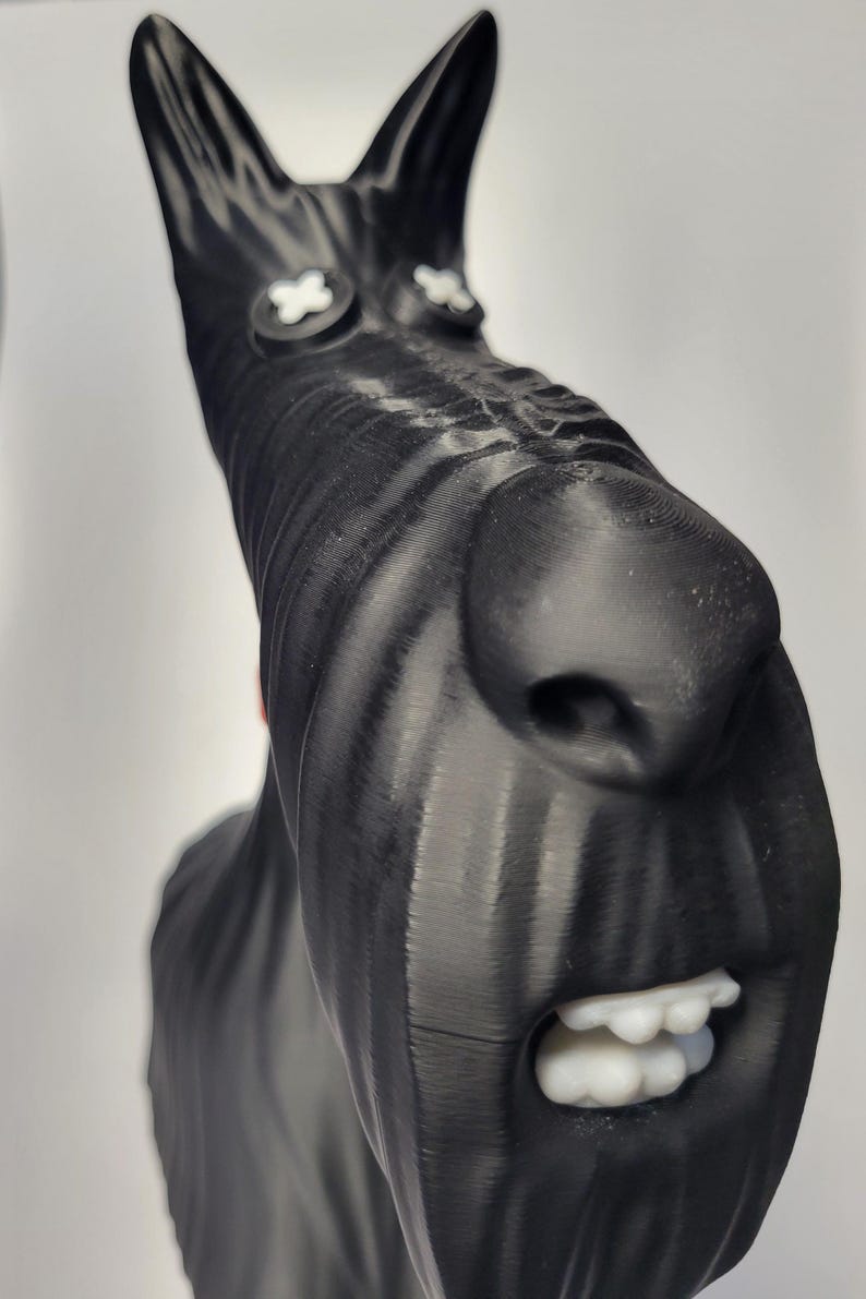 May include: A black sculpture of a dog's head with white accents. The dog has a long snout, large nose, and open mouth with white teeth. The eyes are white crosses. The sculpture is likely 3D-printed.
