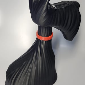 May include: A black decorative sculpture of a Scottish Terrier dog with an orange collar. The dog has a textured coat and is posed in a standing position. The sculpture is made of a solid material and is set against a white background.