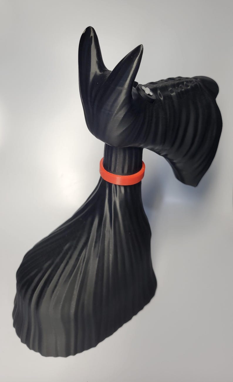 May include: A black decorative sculpture of a Scottish Terrier dog with an orange collar. The dog has a textured coat and is posed in a standing position. The sculpture is made of a solid material and is set against a white background.