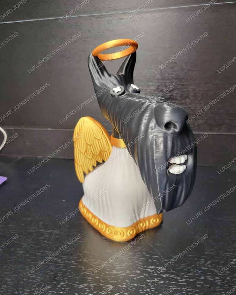 May include: A 3D-printed sculpture of a dog with angel wings and a halo. The dog is black with white teeth and a white chest. The wings and halo are gold, and the base is white with gold trim. The sculpture is a unique decorative item.