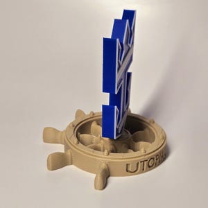 Peut inclure: Un logo bleu imprim&eacute; en 3D d'un gouvernail de navire avec le mot "Utopia" sur la base. Le logo est mont&eacute; sur un gouvernail de navire imprim&eacute; en 3D de couleur beige.