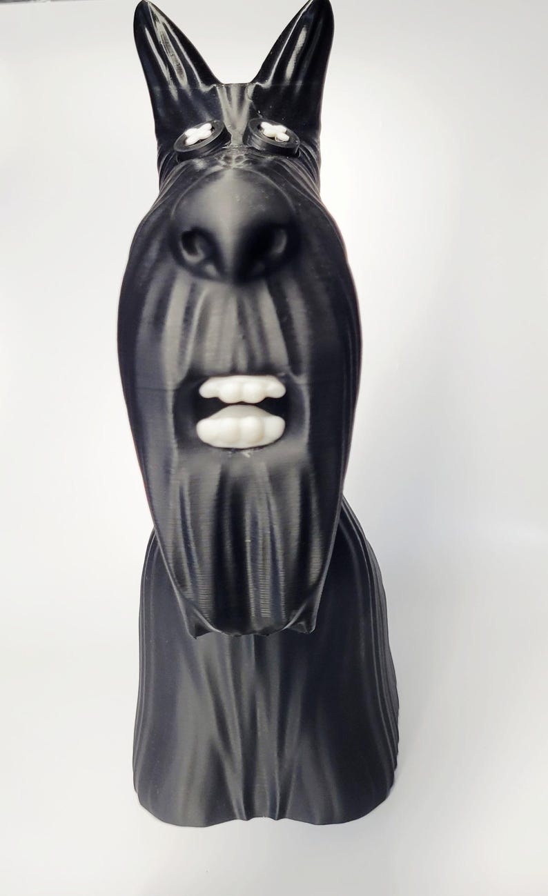 May include: A black sculpture of a Scottish Terrier dog with white teeth and eyes. The dog has a long, textured snout and pointed ears. The sculpture is set against a white background.