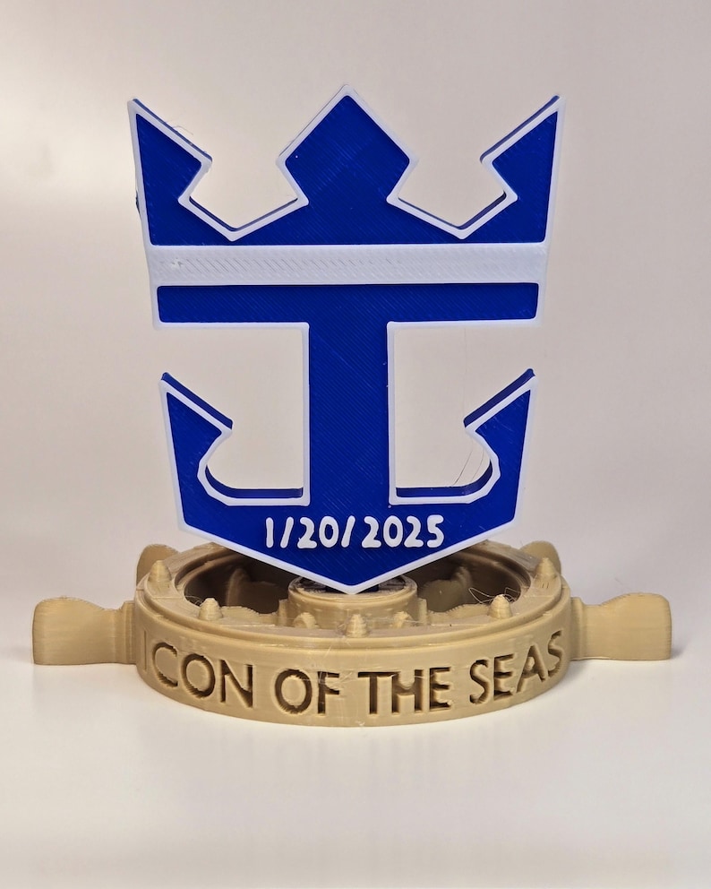 Peut inclure: Un logo de bateau de croisi&egrave;re Royal Caribbean imprim&eacute; en 3D bleu et blanc avec une couronne et une ancre. Le logo est mont&eacute; sur une base en 3D imprim&eacute;e marron avec les mots "CON OF THE SEAS" et la date "1/20/2025".