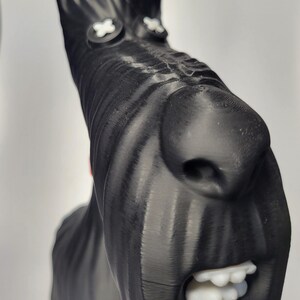 May include: A black sculpture of a dog's head with white accents. The dog has a long snout, large nose, and open mouth with white teeth. The eyes are white crosses. The sculpture is likely 3D-printed.