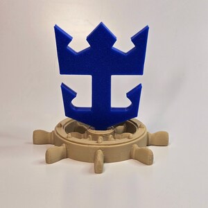 Peut inclure: Un logo Royal Caribbean International imprim&eacute; en 3D de couleur bleue avec une couronne et une ancre, mont&eacute; sur un volant de navire imprim&eacute; en 3D de couleur beige.