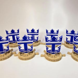 Peut inclure: Huit r&eacute;pliques miniatures imprim&eacute;es en 3D du logo de Royal Caribbean International, repr&eacute;sentant une ancre bleue avec une bande blanche et une couronne dor&eacute;e. Chaque r&eacute;plique est mont&eacute;e sur une base brune avec le texte "Utopia of the Seas" et la date "1/20/2025".