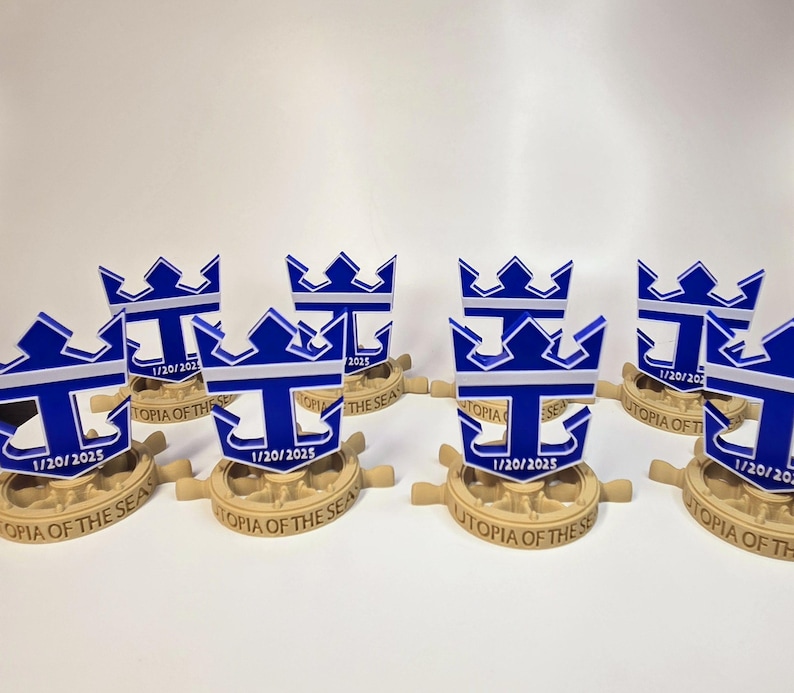Peut inclure: Huit r&eacute;pliques miniatures imprim&eacute;es en 3D du logo de Royal Caribbean International, repr&eacute;sentant une ancre bleue avec une bande blanche et une couronne dor&eacute;e. Chaque r&eacute;plique est mont&eacute;e sur une base brune avec le texte "Utopia of the Seas" et la date "1/20/2025".