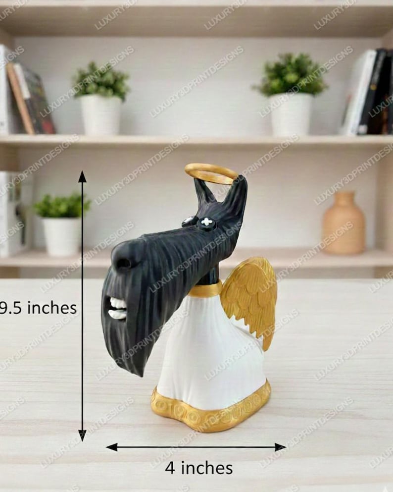 3D printed  Scottie dog figurine from Coraline, with a long black snout, white robe, golden wings, and a gold halo, displayed on a light wooden surface with bookshelves in the background. Measurement labels show 9.5 inches tall and 4 inches wide.”