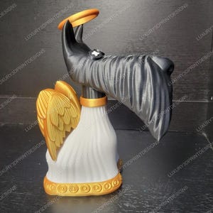 May include: A 3D-printed sculpture of an angel dog with a halo. The dog has a black head and body, gold wings, and a white base. A gold ring is held above the dog's head. The base has a gold trim.
