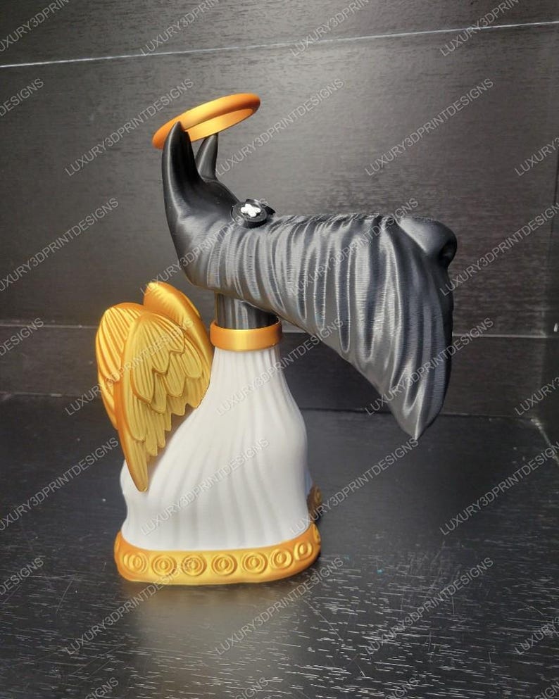 May include: A 3D-printed sculpture of an angel dog with a halo. The dog has a black head and body, gold wings, and a white base. A gold ring is held above the dog's head. The base has a gold trim.