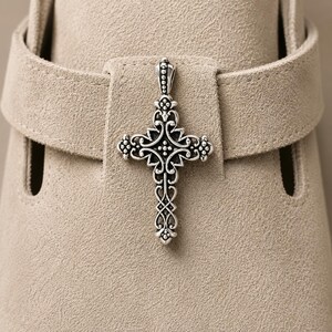 Peut inclure: Un pendentif en argent en forme de croix, avec un design orné et détaillé. La croix est mise en valeur sur un fond neutre, soulignant ses motifs complexes et ses courbes délicates. Le design du pendentif comprend des éléments floraux et en forme de volutes.