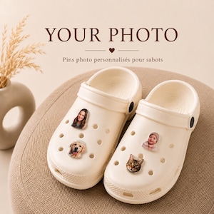 Könnte beinhalten: Ein Paar cremefarbene Schaumstoff-Clogs mit vier individuellen Foto-Pins in den Belüftungslöchern. Die Pins zeigen eine Person, einen Golden Retriever, ein Baby und eine Katze. Über den Schuhen steht der Text YOUR PHOTO und Pins photo personnalisés pour sabots.