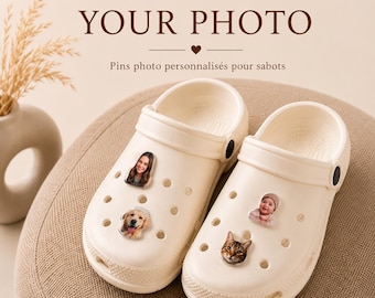 Op de afbeelding: Een paar crèmekleurige schuimrubberen klompen met vier aangepaste fotopins in de ventilatiegaten. De pins tonen een persoon, een golden retriever, een baby en een kat. Boven de schoenen staat de tekst YOUR PHOTO en Pins photo personnalisés pour sabots.