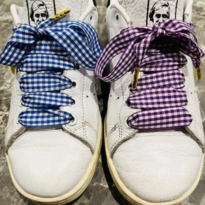 May include: A pair of white leather sneakers with blue and purple gingham ribbon laces. The laces are tied in a bow on each shoe.
