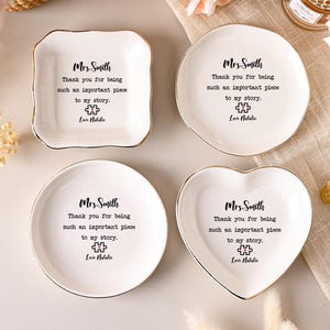 May include: Four white ceramic trinket dishes in square, round, and heart shapes with gold-toned rims. Each dish features the black printed text: Mrs. Smith, Thank you for being such an important piece to my story, a puzzle piece icon, and Love Natalie.
