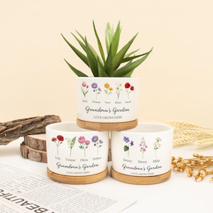 May include: Three white ceramic flower pots with bamboo bases. Each pot features a different arrangement of colourful flowers and the text "Grandma's Garden" with the names of family members below the flowers. The text "Love Grows Here" is printed below the name of the garden.