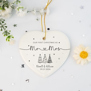 May include: White heart-shaped ceramic ornament with black text that reads "Our first Christmas as Mr & Mrs Kent & Alice 09.21.2024". The ornament features a stylized drawing of three Christmas trees.