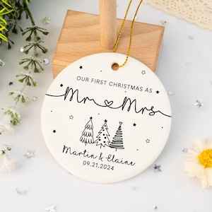 May include: White ceramic Christmas ornament with black text that reads "Our First Christmas as Mr. & Mrs. Martin & Elaine 09.21.2024". The ornament features three stylized Christmas trees.