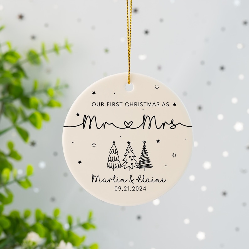 May include: White ceramic Christmas ornament with black text that reads "Our first Christmas as Mr. & Mrs. Martin & Elaine 09.21.2024". The ornament features three stylized Christmas trees with stars.