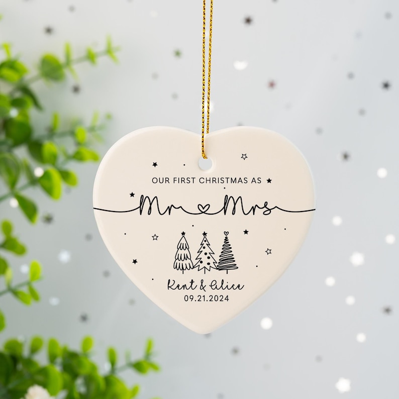 May include: White heart-shaped ceramic ornament with black text and illustrations. The text reads "Our first Christmas as Mr & Mrs Rent & Alice 09.21.2024". The illustration shows three stylized Christmas trees.