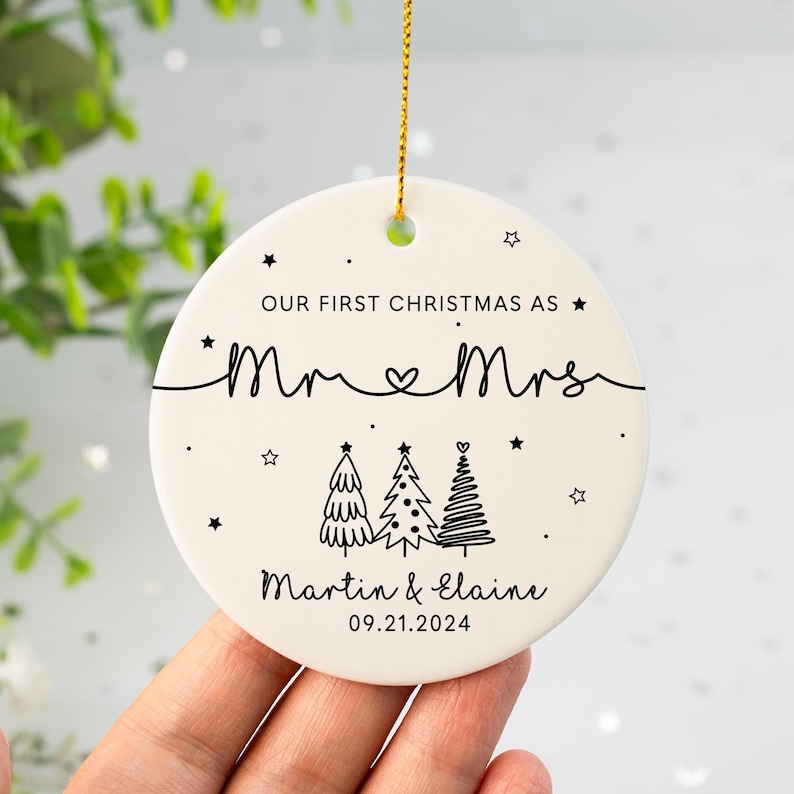 May include: White ceramic Christmas ornament with black text that reads "Our First Christmas as Mr & Mrs Martin & Elaine 09.21.2024". The ornament features three stylized Christmas trees.