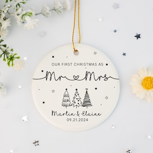May include: White ceramic Christmas ornament with black text that reads "Our First Christmas as Mr. & Mrs. Martin & Elaine 09.21.2024". The ornament features three stylized Christmas trees and stars.