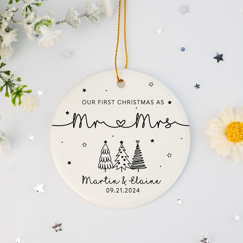 May include: White ceramic Christmas ornament with black text that reads "Our First Christmas as Mr. & Mrs. Martin & Elaine 09.21.2024". The ornament features three stylized Christmas trees and stars.