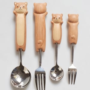 May include: Set of three wooden handled utensils with animal faces. The utensils include a spoon and two forks. The handles are brown and the utensils are silver.