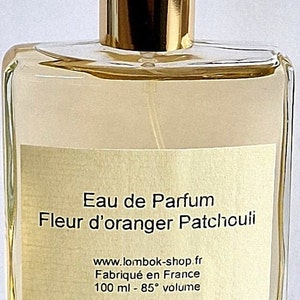 Puede incluir: Una botella de vidrio transparente de Eau de Parfum Fleur d'oranger Patchouli, con un tapón dorado. La botella está etiquetada con el nombre del producto, el sitio web y "Fabriqué en France 100 ml - 85° volume".