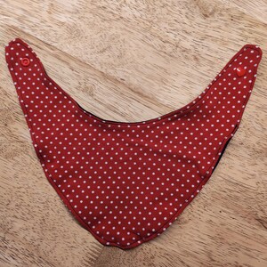 May include: A red and white polka dot bib with a rounded bottom and two red buttons at the top corners. The bib is made of fabric and is designed to catch food and spills.