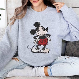 May include: A gray sweatshirt with a cartoon image of Mickey Mouse in a red and black outfit. Mickey Mouse is smiling and has his hands on his hips.