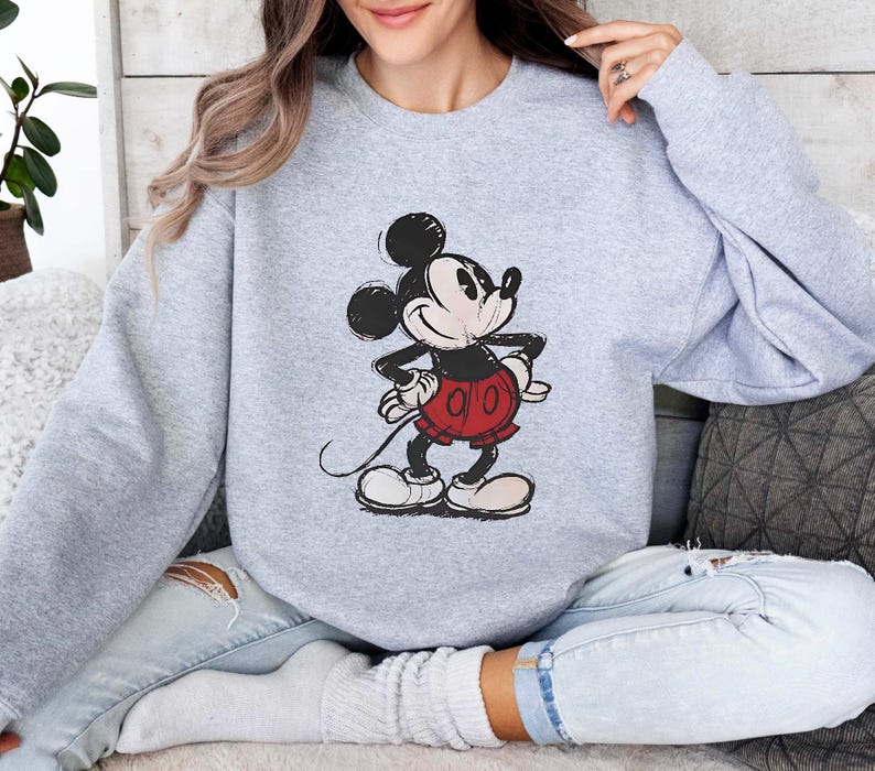 May include: A gray sweatshirt with a cartoon image of Mickey Mouse in a red and black outfit. Mickey Mouse is smiling and has his hands on his hips.
