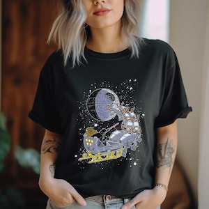 May include: A black t-shirt with a graphic of Darth Vader in a sleigh pulled by AT-ATs flying past the Death Star. The graphic is in a cartoon style and has a festive feel.