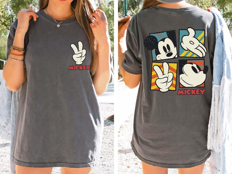 Pode incluir: Uma camiseta cinza com um design vintage do Mickey Mouse. O design apresenta o rosto do Mickey, a m&atilde;o fazendo um sinal de paz e a palavra "Mickey" em vermelho.
