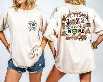 May include: Beige t-shirt with a festive design. The front features the text "Joy to the World" in a circular wreath. The back displays a colorful graphic with Disney characters and holiday elements. A fun, casual top for the holiday season.