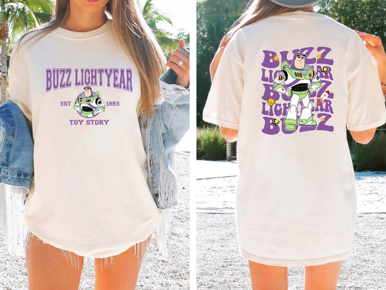 May include: A white t-shirt with a purple and green graphic of Buzz Lightyear from Toy Story. The front of the shirt says "Buzz Lightyear Est. 1995 Toy Story". The back of the shirt has a repeated graphic of Buzz Lightyear with the words "Buzz Lightyear" in a purple, retro font.