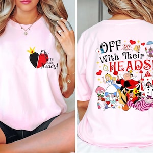 May include: Light pink t-shirt featuring a heart design with a crown and the text "Off With Their Heads!" on the front. The back of the shirt displays a colorful graphic of characters from Alice in Wonderland.