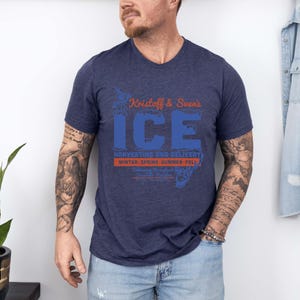 May include: Navy blue V-neck t-shirt with the text "Kristoff & Sven's ICE" in blue and orange. The shirt also features the text "Harvesting and Delivery" and "Winter, Spring, Summer, Fall".