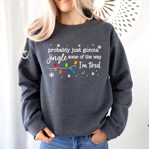 May include: Dark gray sweatshirt with the text "probably just gonna jingle some of the way I'm tired." The text is in white, with colorful Christmas lights and snowflakes. The sweatshirt is a crew neck style.