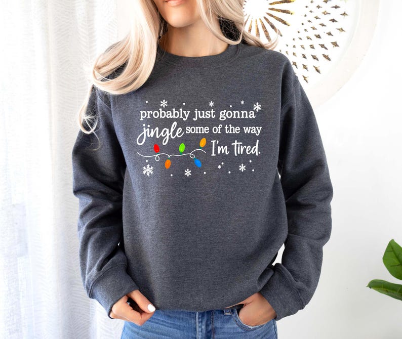 May include: Dark gray sweatshirt with the text "probably just gonna jingle some of the way I'm tired." The text is in white, with colorful Christmas lights and snowflakes. The sweatshirt is a crew neck style.