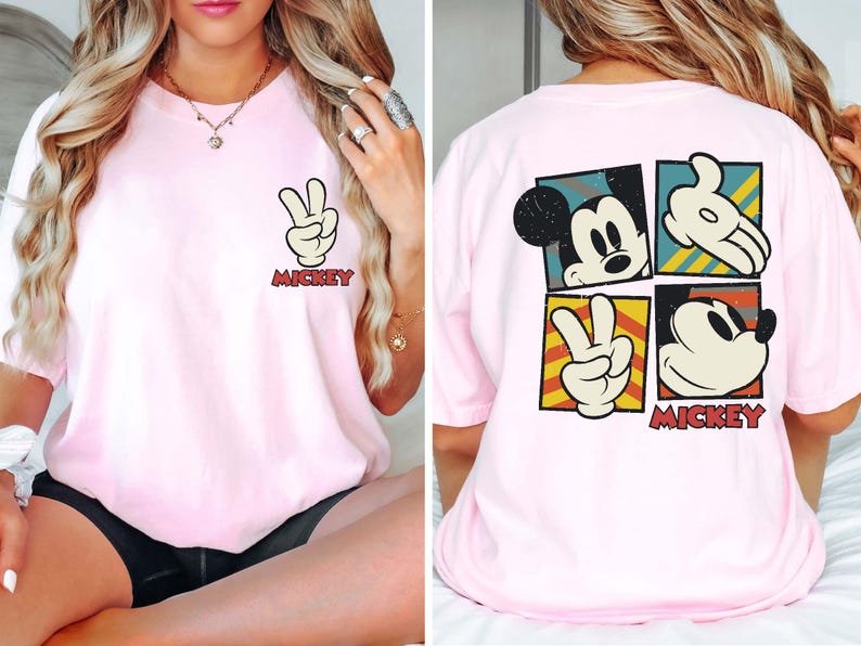 Pode incluir: Camiseta rosa com um gr&aacute;fico do Mickey Mouse na frente e um gr&aacute;fico do Mickey Mouse maior nas costas. O gr&aacute;fico nas costas apresenta o rosto do Mickey Mouse, uma m&atilde;o fazendo um sinal de paz e outra m&atilde;o fazendo um sinal de paz. O texto "Mickey" est&aacute; impresso abaixo do gr&aacute;fico.
