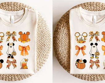 May include: Two white t-shirts with a variety of fall-themed Disney characters and designs. The designs include pumpkins, Mickey Mouse ears, ghosts, and bows.