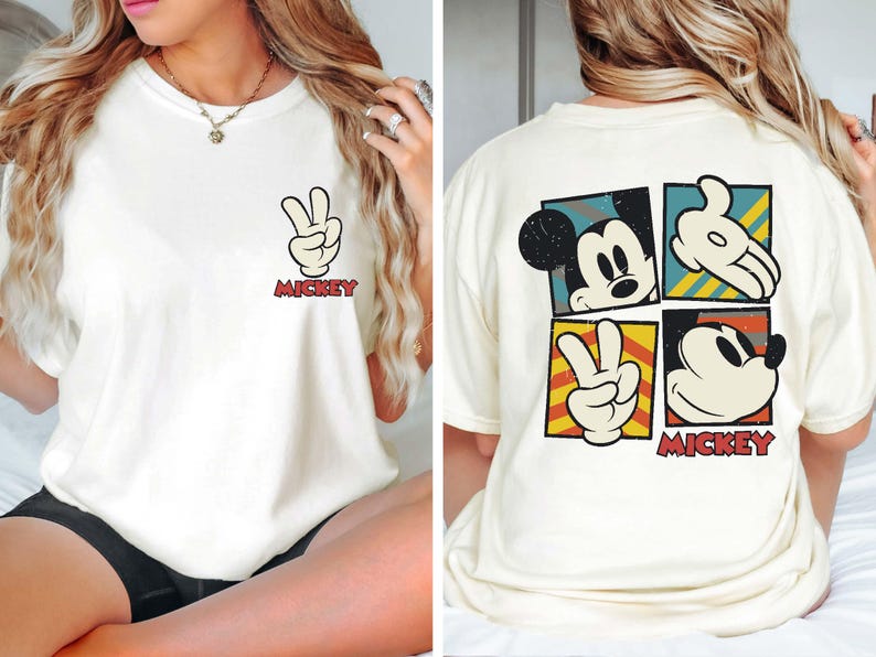 Pode incluir: Camiseta branca com um gr&aacute;fico do Mickey Mouse na frente e nas costas. O gr&aacute;fico da frente &eacute; uma &uacute;nica m&atilde;o do Mickey Mouse fazendo um sinal de paz com o texto "Mickey" abaixo. O gr&aacute;fico das costas &eacute; uma colagem de quatro imagens do Mickey Mouse, incluindo um sinal de paz, uma cabe&ccedil;a do Mickey Mouse e uma m&atilde;o do Mickey Mouse fazendo um sinal de paz. O texto "Mickey" est&aacute; abaixo da colagem.