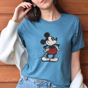 May include: A blue t-shirt with a vintage Mickey Mouse graphic. Mickey is wearing red shorts and is standing with his right hand on his hip.