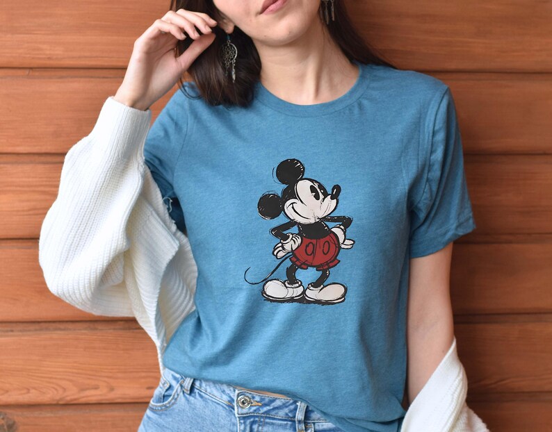 May include: A blue t-shirt with a vintage Mickey Mouse graphic. Mickey is wearing red shorts and is standing with his right hand on his hip.
